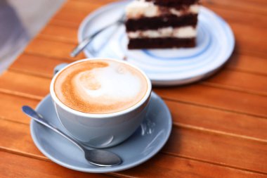 Bir fincan aromatik kahve ve bir dilim kek ahşap masada, yakın plan.