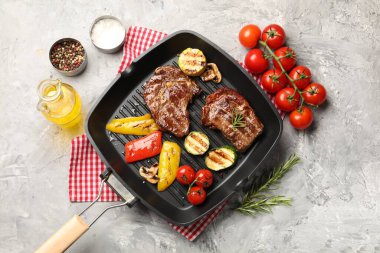 Izgara biftek, mantar, sebze ve baharatlı tava. Gri desenli masa, düz uzanma.