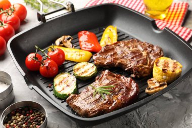 Izgara biftek, mantar, sebze ve baharatlı tava. Gri desenli masa, yakın plan.