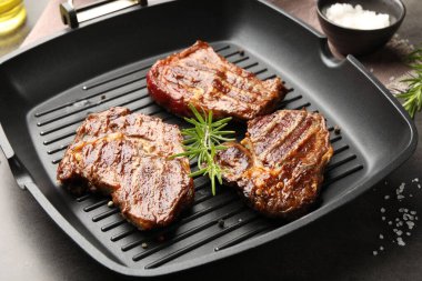 Izgara biftek, biberiye ve tuzlu gri desenli masa, yakın plan.