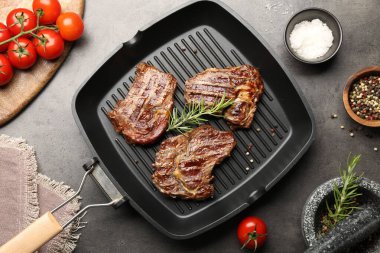 Izgara biftekli tava, biberiye, domates ve baharatlar gri desenli masa, düz uzanma