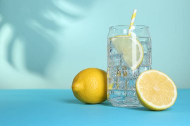 Bardakta buzlu limon suyu ve açık mavi arka planda taze narenciye meyvesi. Metin için boşluk