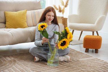 Genç kız evdeki vazoya güzel ayçiçekleri koyuyor.