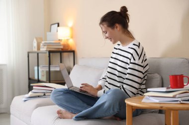 Bilgisayarlı gülümseyen öğrenci evdeki koltukta sınava hazırlanıyor.