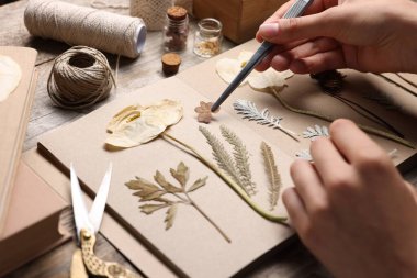 Ahşap masadaki kuru çiçekleri deftere koyan kadın, yakın plan.