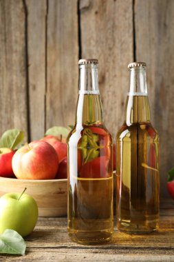 Cam şişelerde nefis elma şarabı ve tahta masada elmalar.