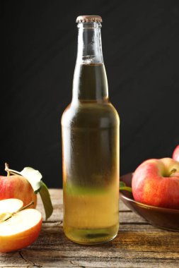 Cam şişede nefis elma şarabı ve ahşap masada koyu gri arka planda elmalar, yakın plan