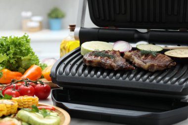 Electric grill with tasty meat and vegetables on table in kitchen, closeup