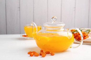 Sea buckthorn tea and fresh berries on white wooden table, closeup
