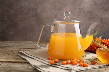 Cam çaydanlıkta deniz dikenli çay, ahşap masada bal ve taze böğürtlen, yakın plan. Metin için boşluk