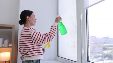 Pencereyi temizleyen kadın, kapalı alanda deterjan, kamera hareket ediyor.