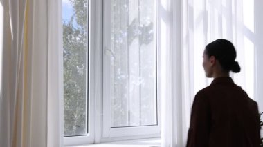Genç bir kadın evinde modern bir pencere açıyor.