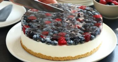 Siyah ahşap masada meyveli kek kesen kadın, yakın plan.