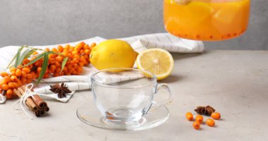 Açık gri masada tatlı deniz dikenli çayını bardağa dolduran kadın, yakın plan.