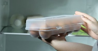 Dolapta çiğ tavuk yumurtası taşıyan bir kadın var.