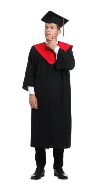 Mezuniyet elbisesi ve beyaz arka planda havan topu giyen düşünceli genç adam.