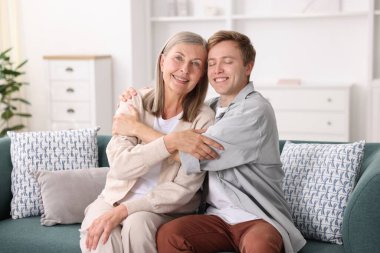 Mutlu oğul ve annesi evde kanepede kucaklaşıyorlar.