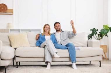 Evdeki koltukta uzaktan kumandayla klima kullanan çift.