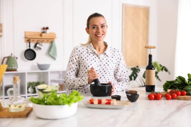 Mutfaktaki masada yemek yapan gülümseyen kadın.