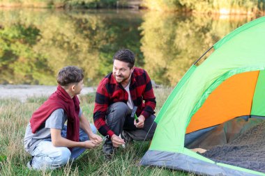 Mutlu baba ve oğul nehir kenarında kamp çadırı kuruyorlar.