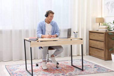 Kulaklıklı bir adam, içerideki masada dizüstü bilgisayarla sınavdan geçerken not alıyor.