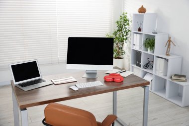 Ofisteki ahşap masada bilgisayar, dizüstü bilgisayar, tablet ve kulaklık ile modern işyeri