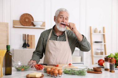 Mutfaktaki beyaz mermer masada yaşlı bir adam yemek pişiriyor.