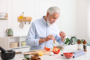 Mutfaktaki beyaz mermer masada yaşlı bir adam yemek pişiriyor.