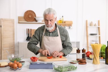 Mutfaktaki beyaz mermer masada yaşlı bir adam yemek pişiriyor.