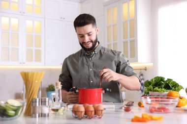 Mutfaktaki masada yemek pişiren gülümseyen adam.