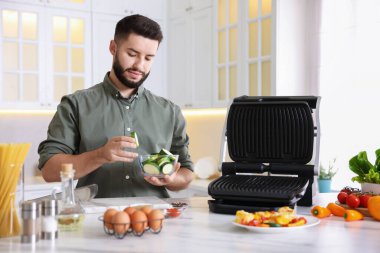 Yemek pişirme süreci. Mutfaktaki masada elektrikli ızgaranın yanında bir kase dilimlenmiş kabakla genç bir adam.