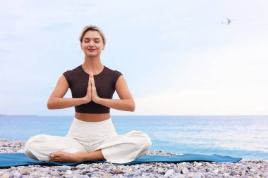 Genç kadın plajda yoga yapıyor, mesaj için yer var.