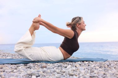 Plajda yoga yapan genç bir kadın.