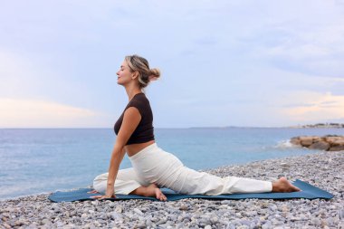 Plajda yoga yapan genç bir kadın.