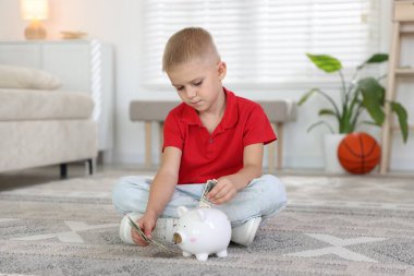 Küçük çocuk evdeki domuz kumbarasına cep harçlığı koyuyor.
