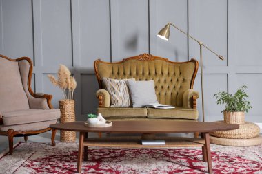 Oturma odasındaki gri duvarın yanında yumuşak kanepe, masa, koltuk ve lamba. İç tasarım