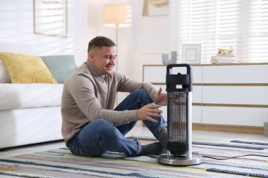 Evdeki elektrikli ısıtıcının yanındaki genç adam.