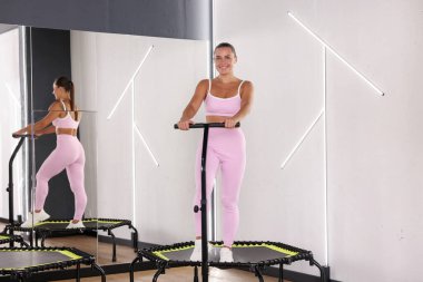Spor salonundaki aynanın yanındaki trambolinde gülümseyen kadın.