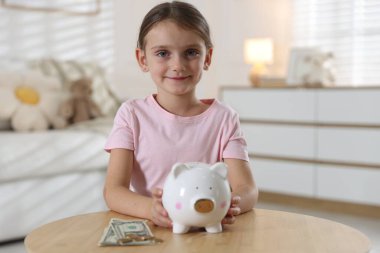 Küçük kız cep harçlığı ve domuz kumbarası ile ahşap masada.