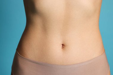 Açık mavi arka planda düz göbekli genç kadın, yakın plan.