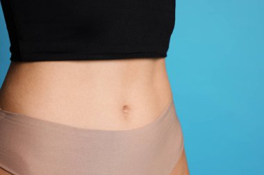 Açık mavi arka planda düz göbekli genç kadın, yakın plan.