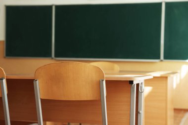 Sınıfta sandalyeli ve yeşil karatahtalı masalar, seçici odaklanma