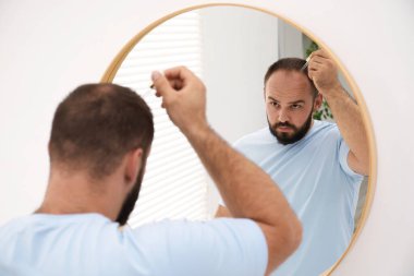 Kellik tedavisi. Evdeki aynanın yanındaki saçına serum süren bir adam.