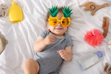 Yatağında güneş gözlüğü ve aksesuarları olan sevimli bir bebek.