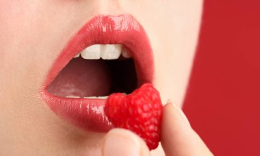 Güzel dudakları makyajlı ve kırmızı arka planda ahududu olan kadın, yakın plan.