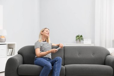 Evdeki kanepede klimalı uzaktan kumandalı bir kadın. Metin için boşluk