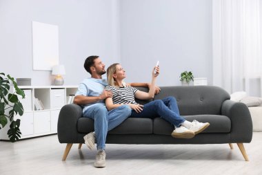 Evdeki koltukta uzaktan kumandayla klima kullanan çift.