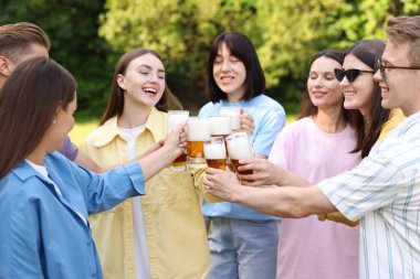 Bir grup mutlu arkadaş dışarıda bira bardaklarını tokuşturuyor.