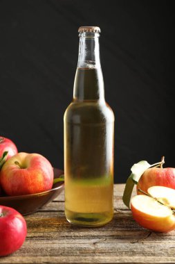 Cam şişede nefis elma şarabı ve ahşap masada koyu gri arka planda elmalar