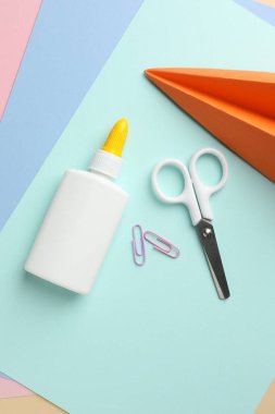 Şişedeki yapıştırıcı, makas, el yapımı uçak ve renkli kağıt üzerine ataç, düz konum